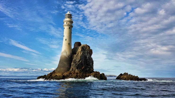 light house lighthouse water island ocean sea mountain sky rock rocks cloud clouds